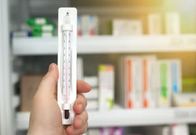 Thermometer vor Medikamentenkühlschrank hochgehalten